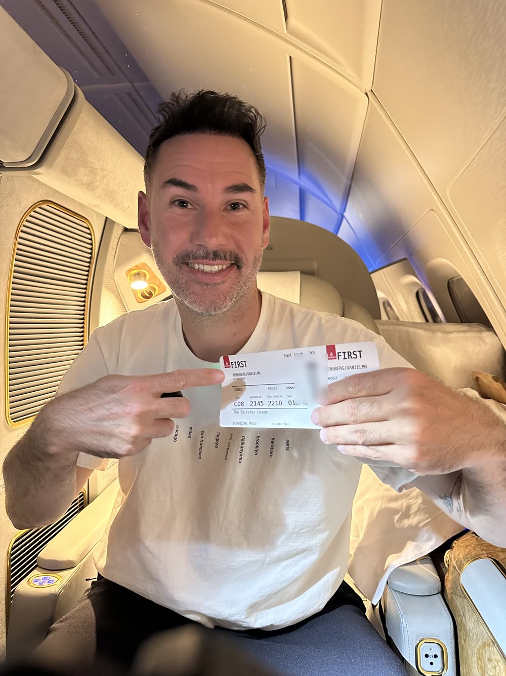 Daniel zeigt lachend seine First-Class-Bordkarte von Emirates