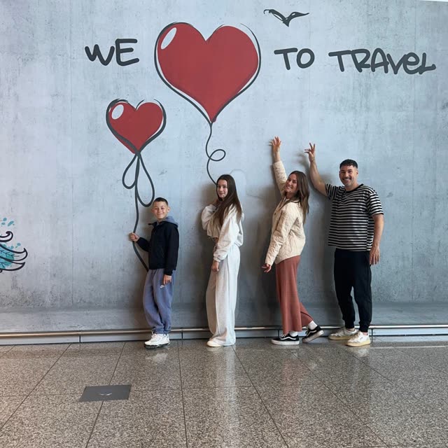 Die ganze Familie am Flughafen Frankfurt vor der Wand „We love to travel“